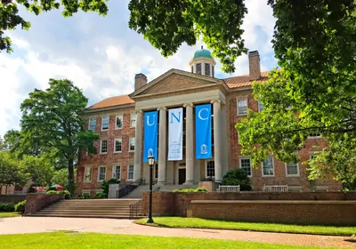Brick building with white pillars and three banners spelling "UNC"
